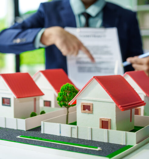 A meeting at an office desk focuses on teamwork with a house mod A meeting at an office desk focuses on teamwork with a house model and discussions on electric cars