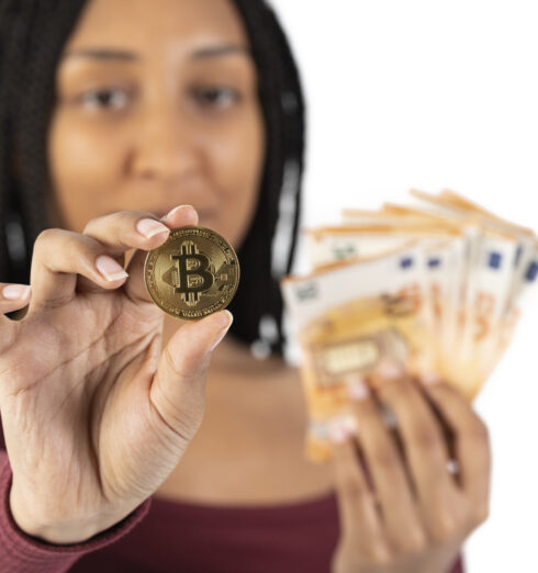 Black woman with some fifty euro bills shows a bitcoin on a white background A young black woman with some fifty euro bills shows a bitcoin coin to the camera on a white background with copy space
